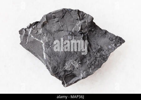 macro shooting of natural mineral rock specimen - raw shungite shale stone on white marble background from Tolvuya district, Karelia, Russia Stock Photo