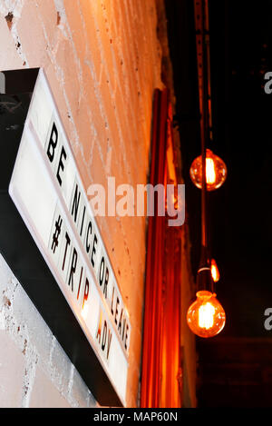 Illuminated sign in restaurant saying ''be nice or leave trip adviser'' on brick wall set against glowing electric light bulbs Stock Photo