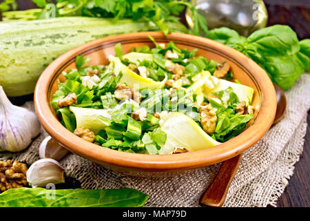 Salad of young zucchini, sorrel, garlic and nuts, seasoned with vegetable oil in clay plate on napkin of sackcloth on a wooden board background Stock Photo