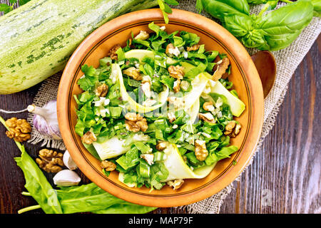Salad of young zucchini, sorrel, garlic and nuts, seasoned with vegetable oil in a plate on napkin of sackcloth on a background of a dark wooden board Stock Photo