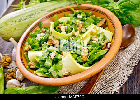 Salad of young zucchini, sorrel, garlic and walnuts, seasoned with vegetable oil in a plate on napkin of sackcloth on a background of dark wooden boar Stock Photo
