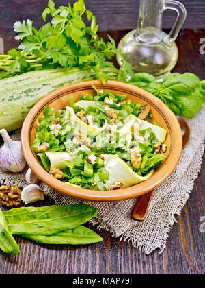 Salad of young zucchini, sorrel, garlic and nuts, seasoned vegetable oil in a plate on napkin of sackcloth on wooden board background Stock Photo