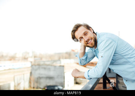 casual handsome blonde man standing outside in blue shirt, smiling and having a positive attitude, looking to camera Stock Photo