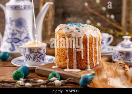 Easter tea, milk is poured into a cup of tea. Fresh homemade cake in sugar icing for the holiday. Easter decorations on the table. Stock Photo
