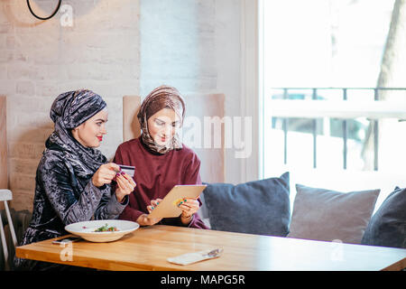 Two Muslim women in cafe, shop online using electronic tablet Stock Photo