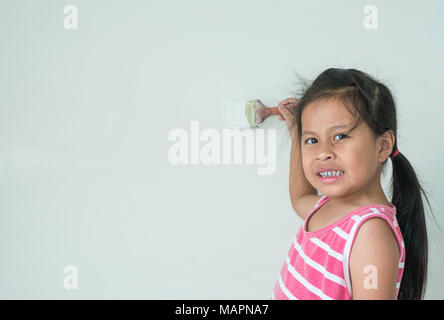 Little a cute girl painting wall and smiling on the white wall background, Stock Photo