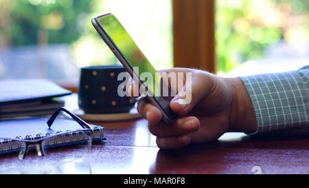 Man using smart phone closeup, at desk backlit by sunshine with reflections through window. Stock Photo
