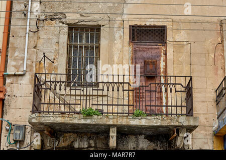a rusty door and barred window opening to a crumbling balcony Stock Photo