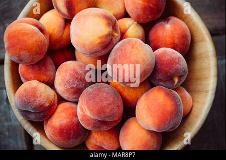 Top down view of a group of ripe peaches in a wooden bowl. Stock Photo