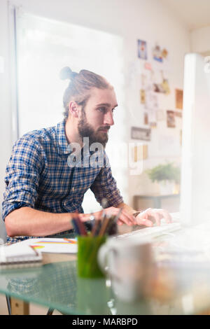 Young man sitting at his desk in front of his computer  Stock Photo