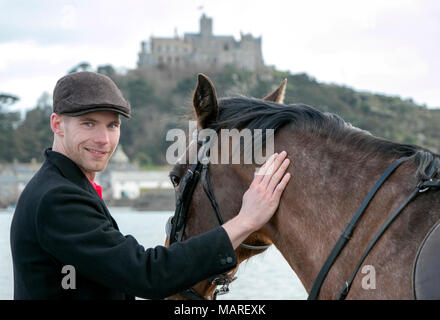 Handsome Male Horse Rider standing walking his horse, wearing flat cap, white trousers and black boots on beach in front of St Michael's Mount Stock Photo