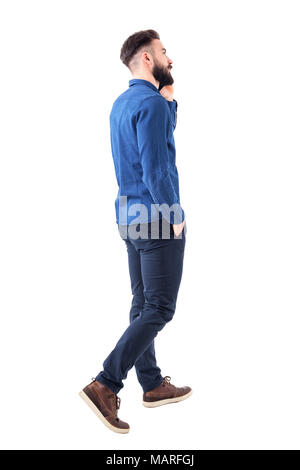 Rear side view of young elegant smart casual business man talking on the phone walking and looking up. Full body isolated on white background. Stock Photo