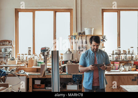 Young carpenter using a digital tablet in his workshop Stock Photo