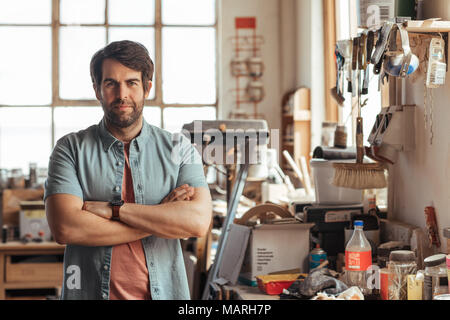 Confident young woodworker standing by a bench in his workshop Stock Photo