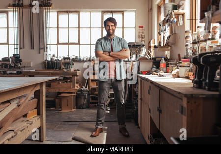 Smiling young woodworker standing in his workshop full of tools Stock Photo