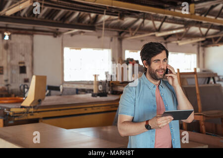 Woodworker using a cellphone and tablet in his workshop Stock Photo