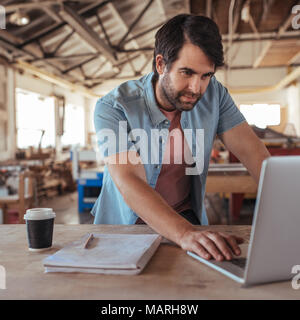 Young woodworker creating new designs on a laptop Stock Photo