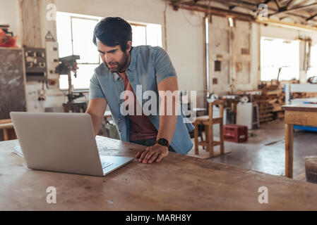 Creative young woodworker creating new designs using a laptop Stock Photo