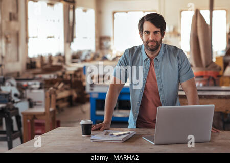 Confident young craftsman using a laptop in his workshop Stock Photo