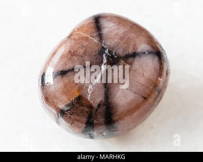 macro shooting of natural mineral rock specimen - tumbled Chiastolite gemstone on white marble background Stock Photo