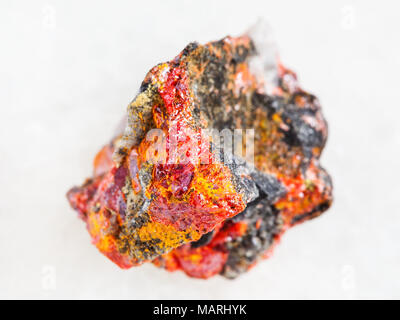macro shooting of natural mineral rock specimen - rough Realgar crystals on stone on white marble background from Luhumi mine, Georgia Stock Photo