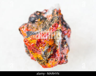 macro shooting of natural mineral rock specimen - raw Realgar crystals on stone on white marble background from Luhumi mine, Georgia Stock Photo