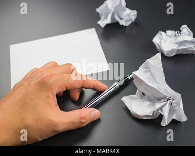 Hand with pen and crumpled paper balls on black background Stock Photo