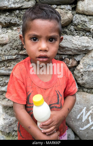 A young boy holds a bottle of milk at the Jesuit feeding program which distributes food to malnourished children in Cocoa village, Ermera, Timor-Leste. Many villagers in the rural areas have large families which they can't support, so a large number of the children suffer from malnutrition. This feeding program is carried out on an almost daily basis at three villages in the Ermera district. Stock Photo