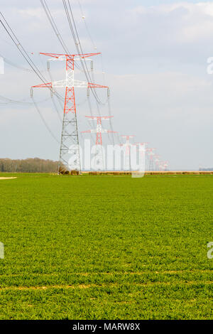 A high-voltage overhead power line supported by red and white transmission towers across the french countryside, with a crop field in the foreground. Stock Photo
