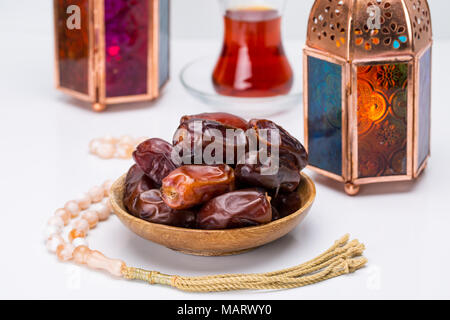Ramadan Kareem Festive, close up of dates on wooden plate and rosary with oriental Lantern lamps and cup of black tea on white background. Islamic Hol Stock Photo