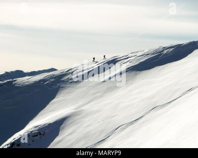 two backcountry skiers hiking up on a long mountain ridge towards the summit near Klosters in the Swiss Alps in deep winter Stock Photo