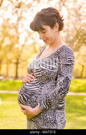 Pregnant woman in a park holding her belly, UK Stock Photo