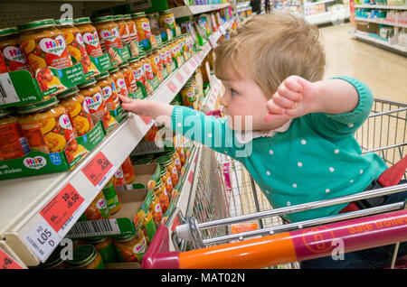 Baby at supermarket reaching for baby food jars, UK Stock Photo