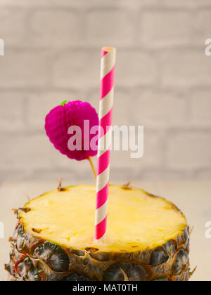 Fresh organic pineapple with a drinking straw on a wooden table Stock Photo