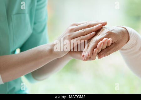 Young caretaker massaging pensioner's hand with Parkinson's disease Stock Photo