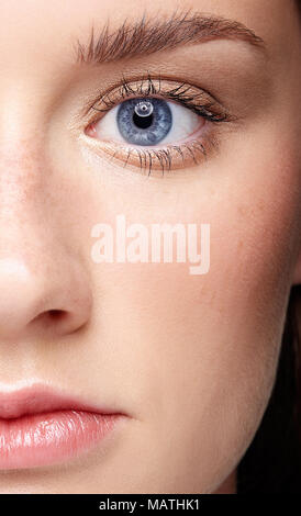 Closeup macro portrait of female face and blue eye. Human woman half-face  with day beauty makeup. Girl with perfect skin and freckles. Stock Photo