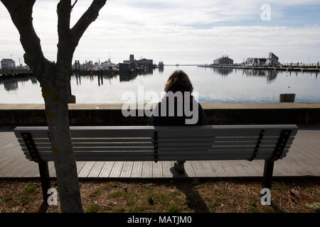 Woman sitting on a bench in the winter off season, Provincetown harbor, Cape Cod, Massachusetts Stock Photo