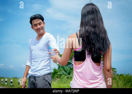 Sport woman giving a bottle of drinking water to a man after exercise. Stock Photo