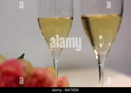 Two champagne flutes / sparkling wine glasses photographed on a white table with a bouquet made of light pink roses. Luxurious celebration! Stock Photo