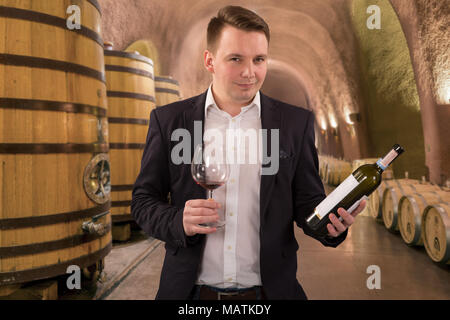 Winemaker or sommelier inspecting quality of red wine, standing near bottles racks in winery vault Stock Photo