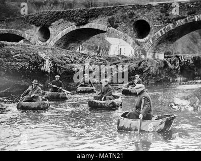 Group of men fishing for salmon in coracles on the River Teifi at Cenarth, on the border of Pembrokeshire, Ceredigion, and Carmarthenshire in Wales. Black and white photograph. The Cenarth Bridge, or Pont Canarth in Welsh, in the background. Mid 20th century. Stock Photo