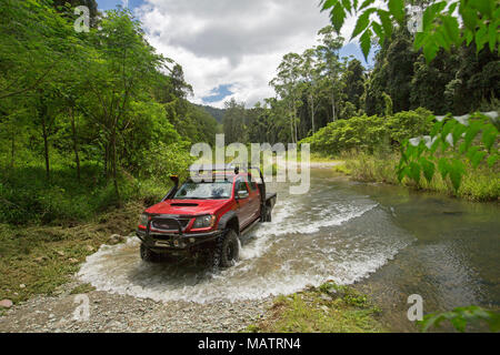 Red four wheel drive vehicle crossing creek hemmed with emerald forests in Conondale Ranges National Park Queensland Australia Stock Photo