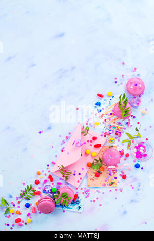 Party invitation concept. Love letter in a pink envelop with macarons, candies and confetti on a light background with copy space. Stock Photo