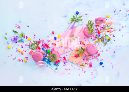 Party invitation concept. Love letter in a pink envelop with macarons, candies and confetti on a light background with copy space. Stock Photo