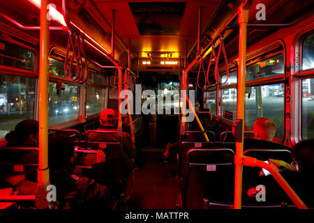 People riding a Portland, Oregon TriMet bus at night. The bus is dimly lit red inside to increase visibility, and safety for the bus driver Stock Photo