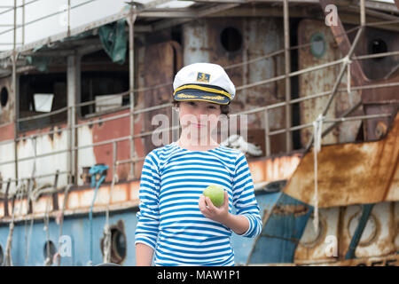 Portrait of a boy in a vest (Telnyashka) and captain's cap. In his hand a green apple. Stock Photo