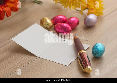Chocolate Easter Eggs Over Wooden background with blessing card with pen and flowers on wood table. Stock Photo