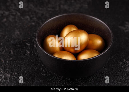 Eggs, painted in gold for the holiday. Golden eggs in a black cup on a black textured background. Easter eggs. Stock Photo