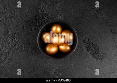 Golden eggs in a black cup on a black textured background. Easter eggs. Stock Photo