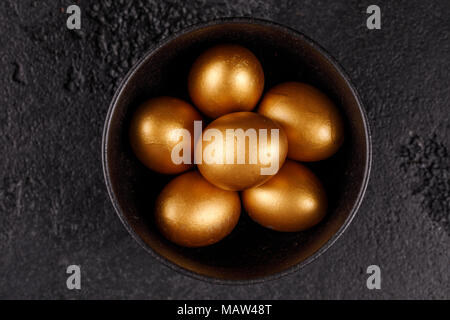 Golden eggs in a black cup on a black textured background. Easter eggs. Stock Photo